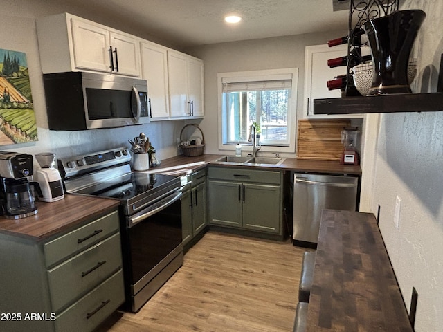 kitchen with light wood finished floors, wooden counters, appliances with stainless steel finishes, white cabinetry, and a sink