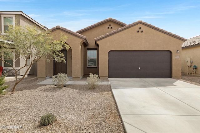 view of front of property featuring a garage, a tile roof, concrete driveway, and stucco siding