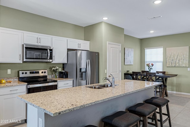 kitchen featuring recessed lighting, a breakfast bar, a sink, white cabinets, and appliances with stainless steel finishes