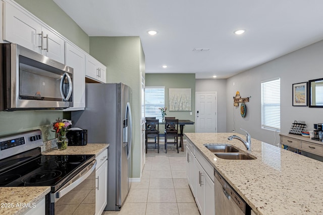 kitchen featuring light stone counters, light tile patterned flooring, stainless steel appliances, a sink, and white cabinets