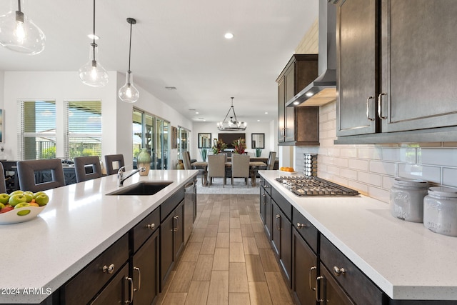 kitchen featuring backsplash, wall chimney range hood, stainless steel appliances, sink, and an island with sink