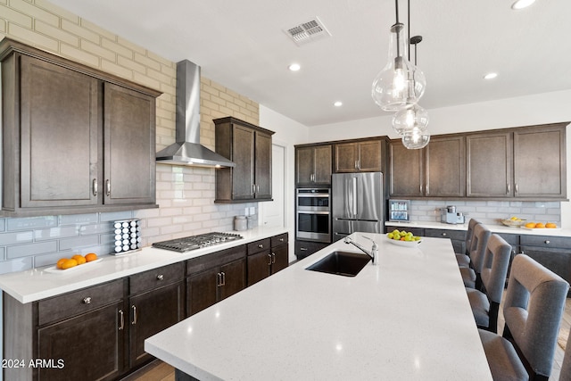 kitchen featuring pendant lighting, backsplash, wall chimney range hood, stainless steel appliances, and sink