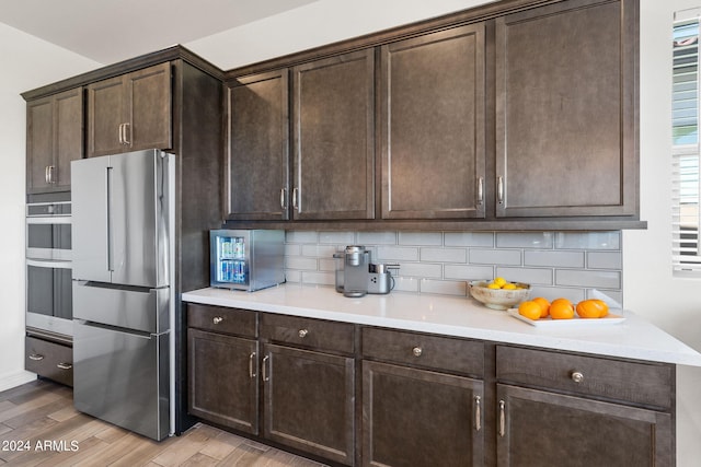 kitchen featuring appliances with stainless steel finishes, dark brown cabinets, light hardwood / wood-style floors, and backsplash