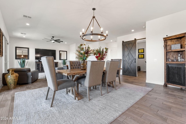 dining space with ceiling fan with notable chandelier, a barn door, and light hardwood / wood-style flooring