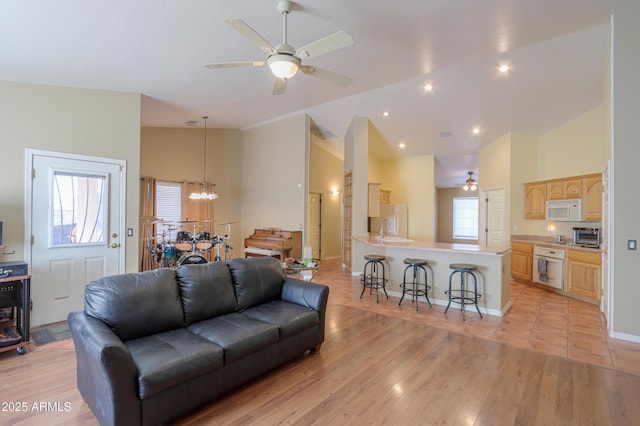 living room featuring ceiling fan with notable chandelier, a healthy amount of sunlight, light hardwood / wood-style floors, and high vaulted ceiling