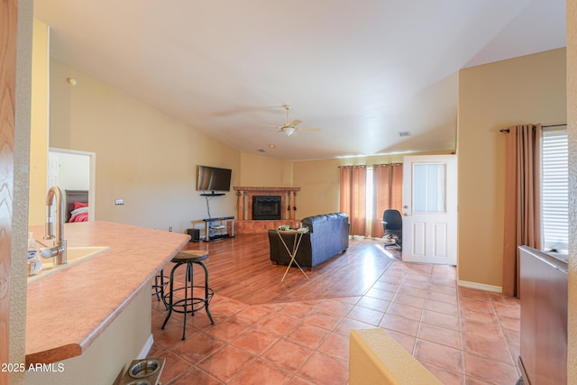 living room with vaulted ceiling, a fireplace, light tile patterned floors, sink, and ceiling fan