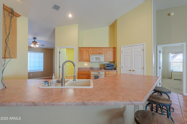 kitchen featuring kitchen peninsula, light brown cabinetry, sink, white appliances, and a breakfast bar