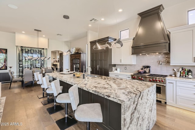 kitchen with a spacious island, white cabinetry, custom range hood, high end stainless steel range oven, and pendant lighting