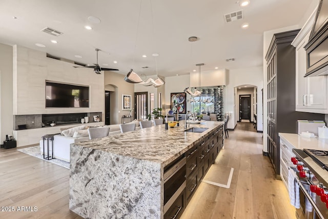 kitchen featuring a center island with sink, arched walkways, high end range, pendant lighting, and a sink