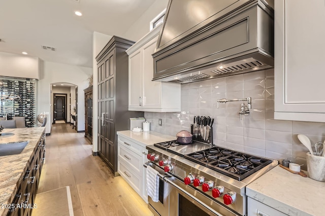 kitchen with arched walkways, high end stove, premium range hood, visible vents, and white cabinetry