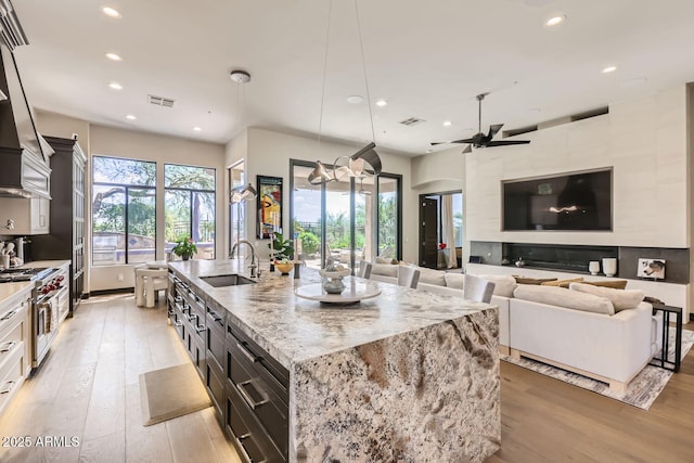 kitchen featuring a sink, open floor plan, hanging light fixtures, double oven range, and a large island with sink