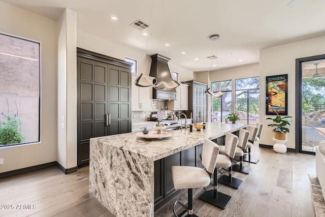 kitchen with light stone counters, a breakfast bar area, a spacious island, visible vents, and pendant lighting