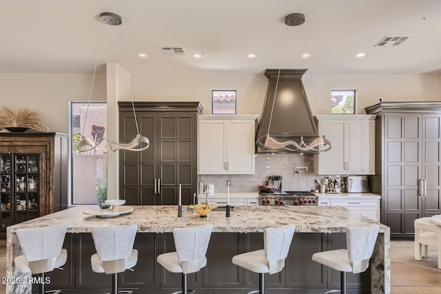 kitchen featuring custom range hood, stove, visible vents, and white cabinetry