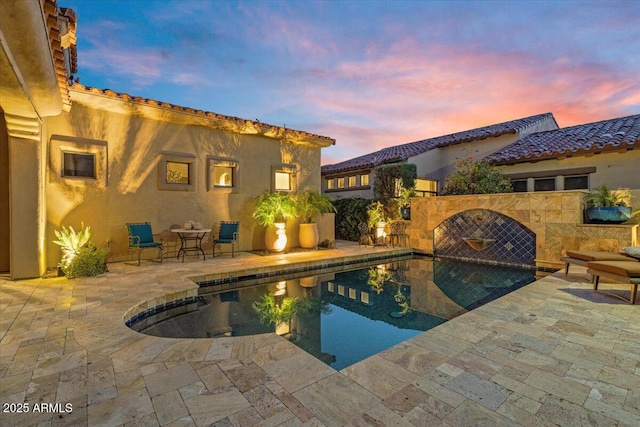 pool at dusk with a patio area and an outdoor pool