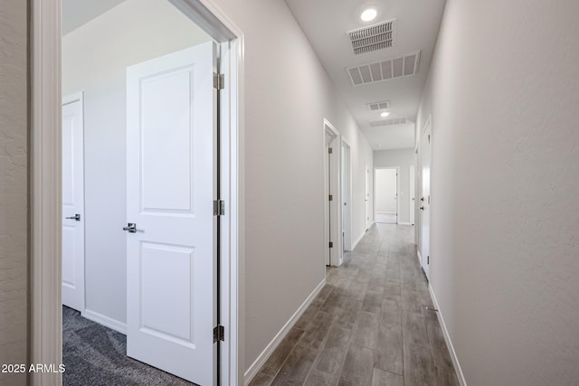 hall with visible vents, baseboards, and wood finished floors
