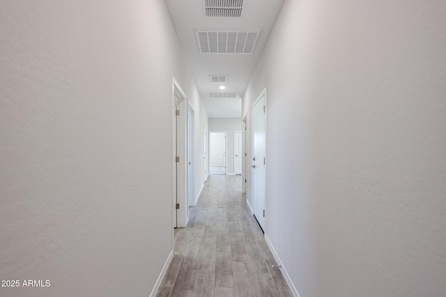 hallway featuring light wood-style floors, visible vents, and baseboards