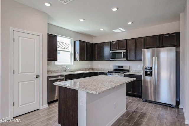 kitchen featuring dark brown cabinetry, wood finish floors, a center island, light stone countertops, and appliances with stainless steel finishes