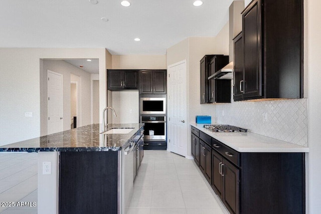 kitchen featuring wall chimney exhaust hood, stainless steel gas cooktop, sink, dark stone countertops, and an island with sink