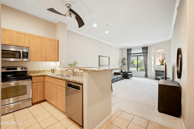 kitchen featuring light brown cabinets, a sink, appliances with stainless steel finishes, a glass covered fireplace, and open floor plan