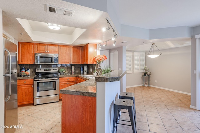 kitchen with a raised ceiling, kitchen peninsula, a breakfast bar area, decorative backsplash, and appliances with stainless steel finishes