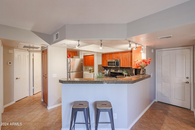 kitchen with rail lighting, stainless steel appliances, backsplash, kitchen peninsula, and a breakfast bar area