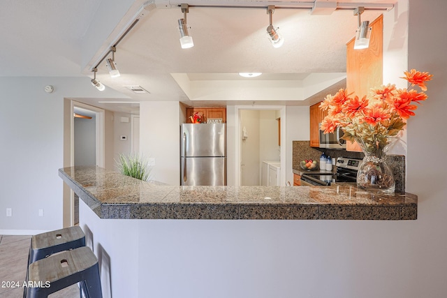 kitchen featuring rail lighting, stainless steel appliances, kitchen peninsula, a kitchen bar, and washer and dryer