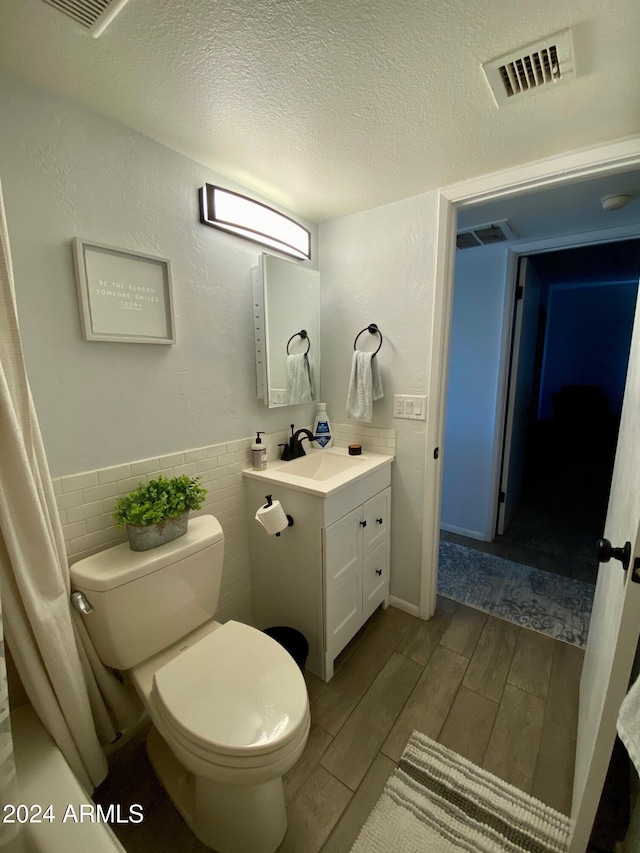 bathroom featuring a textured ceiling, hardwood / wood-style floors, toilet, tile walls, and vanity