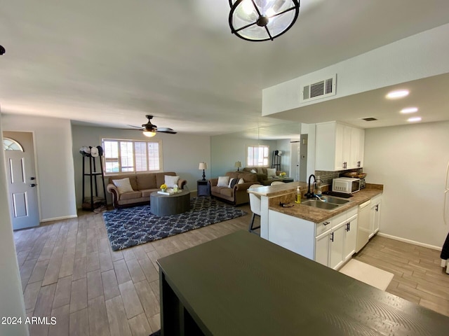 kitchen featuring kitchen peninsula, sink, light wood-type flooring, white cabinetry, and ceiling fan