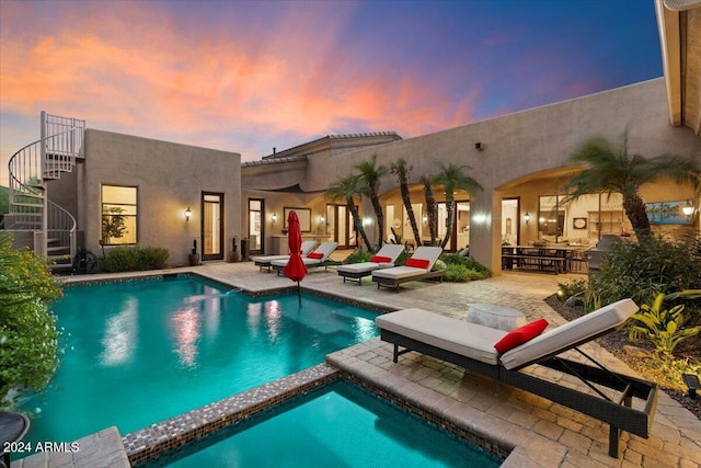 pool at dusk featuring a patio area and an in ground hot tub