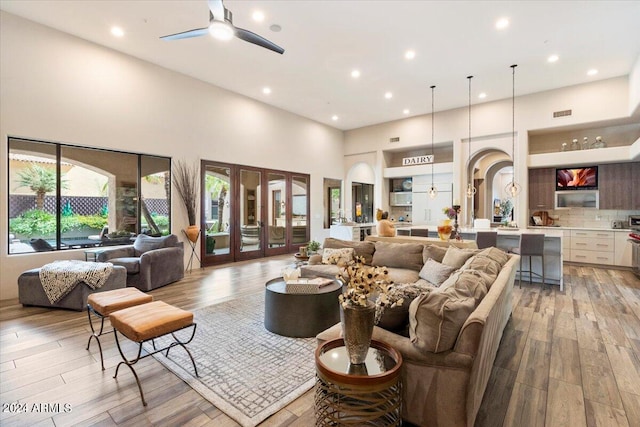 living room with ceiling fan, light hardwood / wood-style floors, and a high ceiling