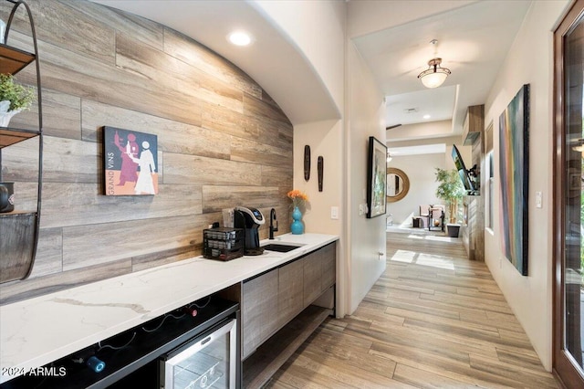 interior space featuring wine cooler, wooden walls, sink, and light wood-type flooring