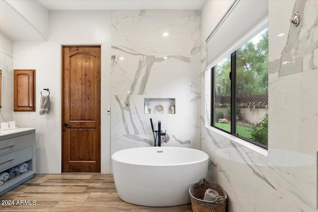 bathroom with a washtub, wood-type flooring, vanity, and tile walls