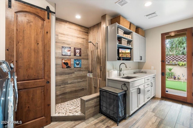 interior space with wooden walls, sink, a barn door, light hardwood / wood-style flooring, and white cabinetry