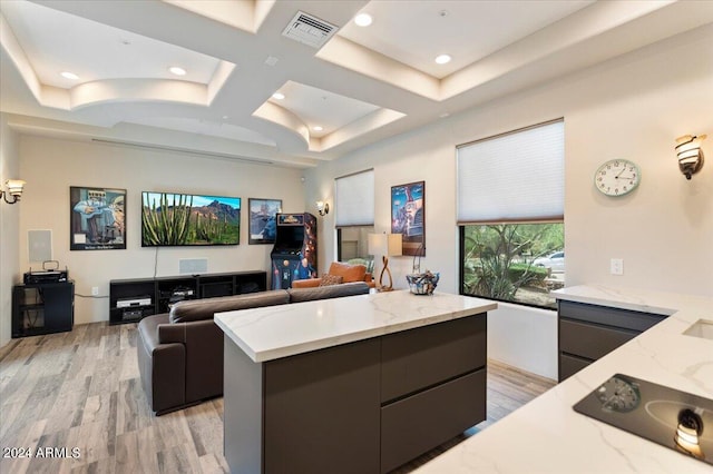 kitchen with coffered ceiling, black electric stovetop, a kitchen island, light stone countertops, and light hardwood / wood-style floors