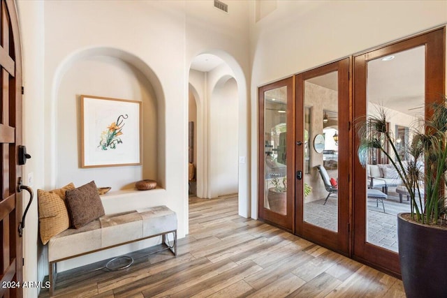 entryway with french doors, a towering ceiling, and light wood-type flooring