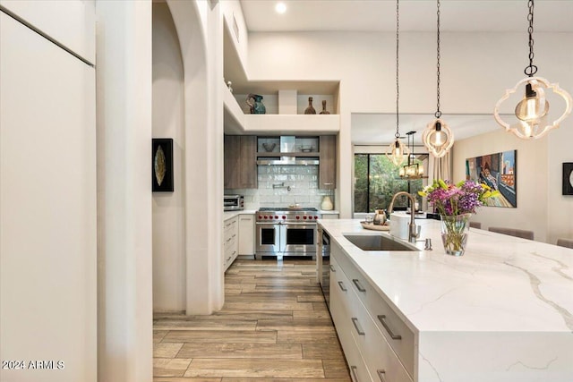 kitchen with white cabinets, sink, an island with sink, light stone counters, and stainless steel appliances