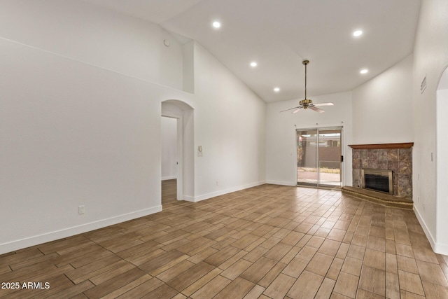 unfurnished living room with baseboards, a fireplace, arched walkways, and ceiling fan