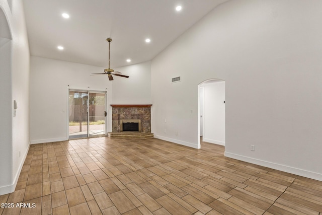 unfurnished living room featuring wood finished floors, visible vents, arched walkways, ceiling fan, and a towering ceiling