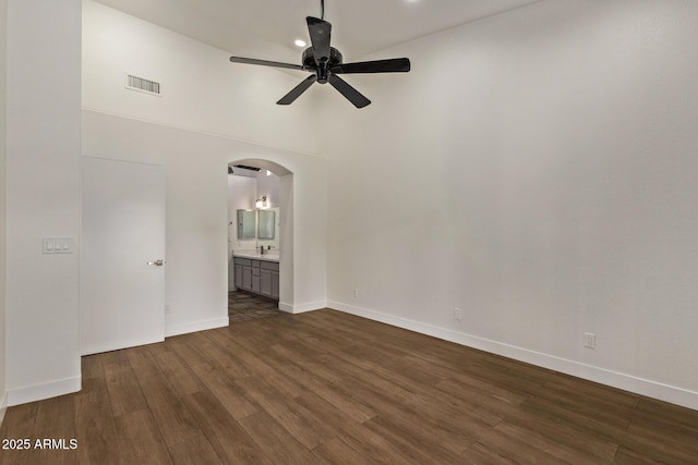 spare room featuring visible vents, dark wood finished floors, a towering ceiling, arched walkways, and a ceiling fan