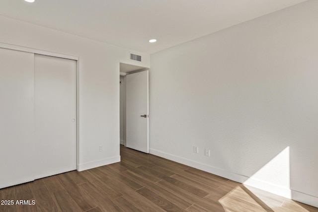 unfurnished bedroom with wood finished floors, visible vents, a closet, and baseboards