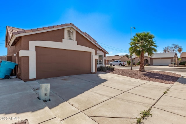 view of side of property featuring stucco siding, a tiled roof, and concrete driveway