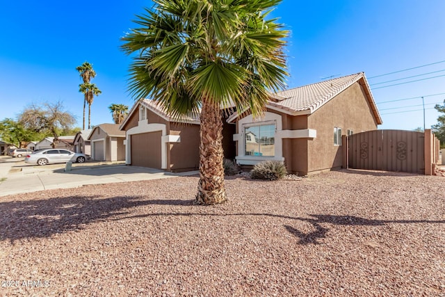 view of front of home featuring concrete driveway, a gate, a tile roof, and stucco siding