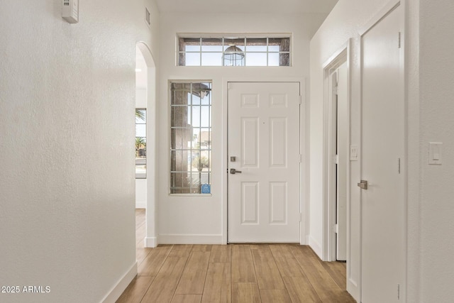 entryway with visible vents, baseboards, light wood finished floors, arched walkways, and a textured wall