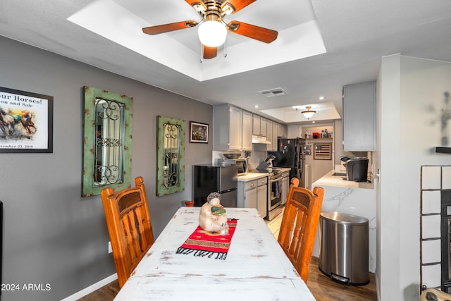 dining area with wood-type flooring, ceiling fan, and a tray ceiling