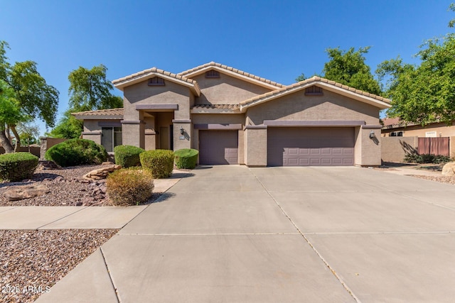 view of front of home featuring a garage, fence, a tile roof, concrete driveway, and stucco siding