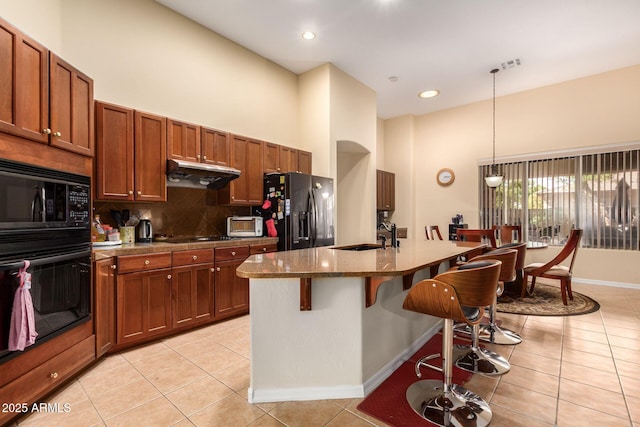 kitchen featuring light tile patterned floors, a breakfast bar area, under cabinet range hood, black appliances, and a sink