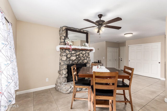 dining room featuring ceiling fan, light tile patterned floors, and a fireplace