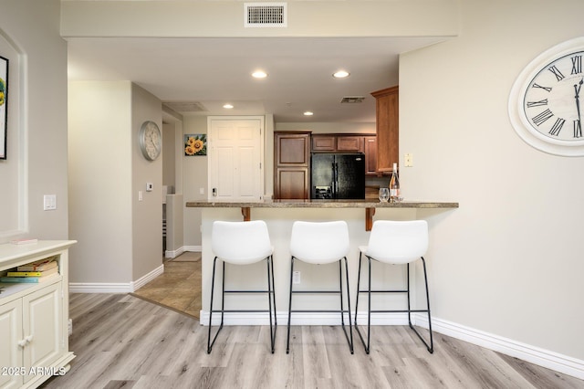 kitchen featuring a breakfast bar area, brown cabinetry, visible vents, light wood-type flooring, and black refrigerator with ice dispenser