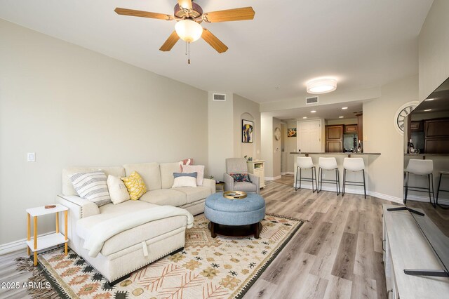 living area with visible vents, ceiling fan, light wood-type flooring, and baseboards