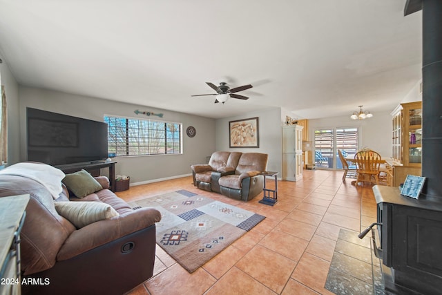 living room with a wood stove, light tile patterned floors, and ceiling fan with notable chandelier